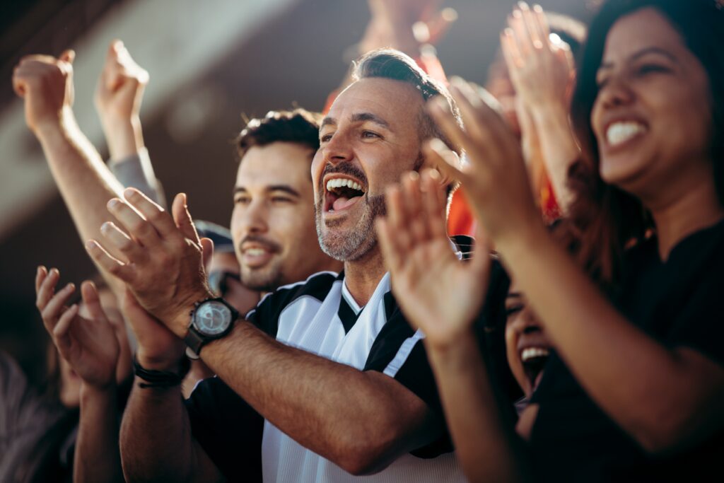 A group of enthusiastic fans cheering and clapping in a stadium.