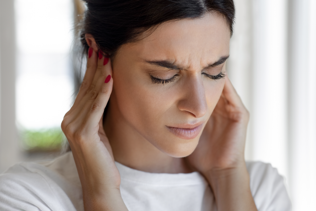 Close-up of a woman holding her hands to her ears, appearing distressed, possibly due to ear discomfort or hearing issues.