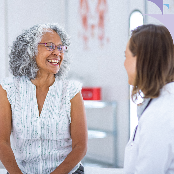 A senior woman smiling while speaking with a hearing care professional about real-ear measurement for hearing aid calibration
