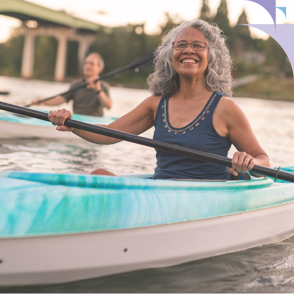 A senior woman smiling while kayaking outdoors, enjoying clear hearing and active living with properly calibrated hearing aids.