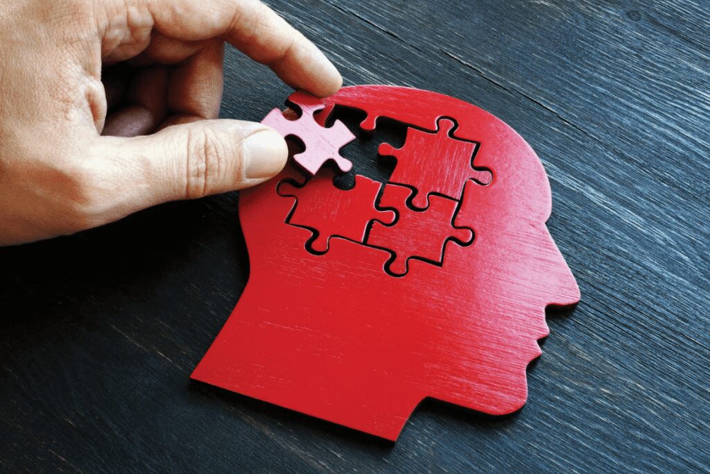 Hand placing a puzzle piece into a red human head silhouette, symbolizing the connection between hearing loss, memory, and cognitive function