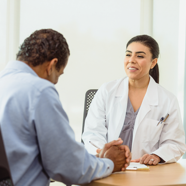 Female audiologist smiling while consulting with a male patient during a hearing care appointment in a clinic setting.
