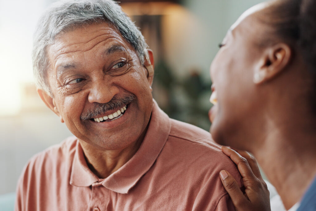 Smiling older man talking with a loved one, symbolizing restored connection through better hearing care.