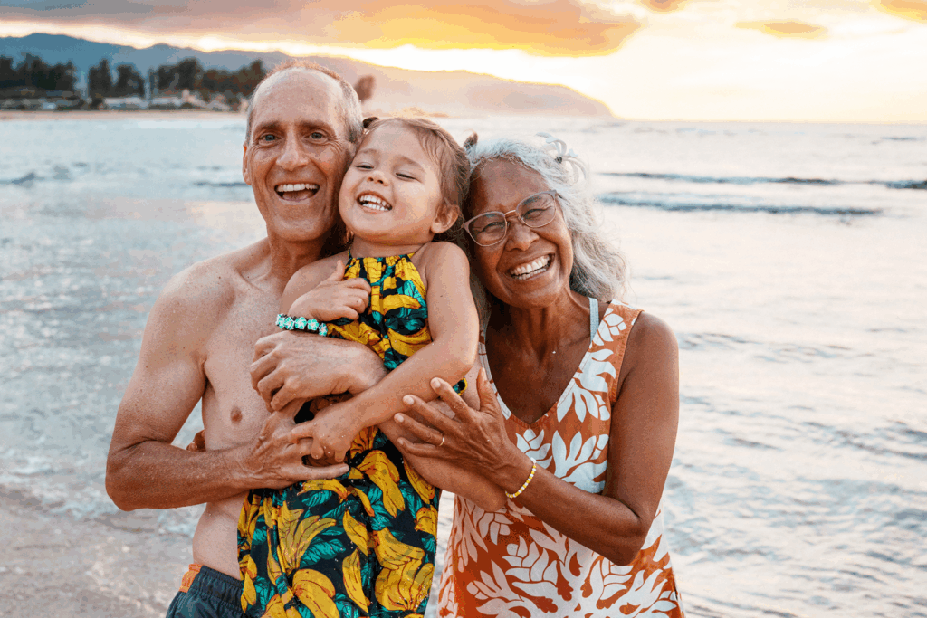Smiling multigenerational family enjoying sunset on a tropical beach, highlighting the joy of staying connected through better hearing.