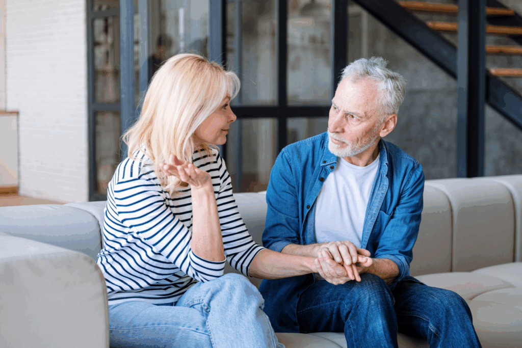 Aging couple sitting on a couch having a serious conversation, representing the emotional and relational impact of hearing loss.