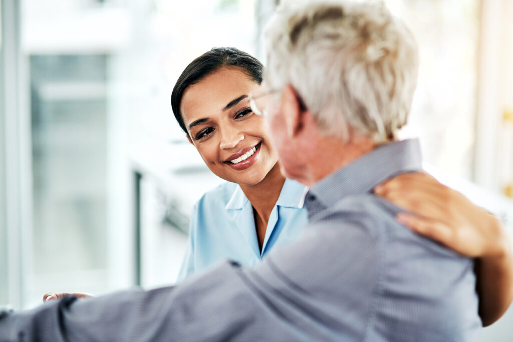 Smiling hearing care provider offering support to an older male patient during a consultation.