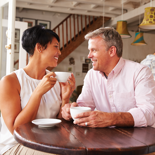 Happy couple sitting at a cafe, smiling and talking over coffee, representing the joy of reconnecting through better hearing.