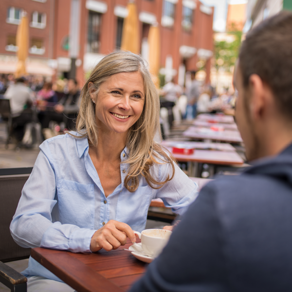 Smiling woman enjoying a conversation at an outdoor café, illustrating confident communication and social connection after improving hearing.