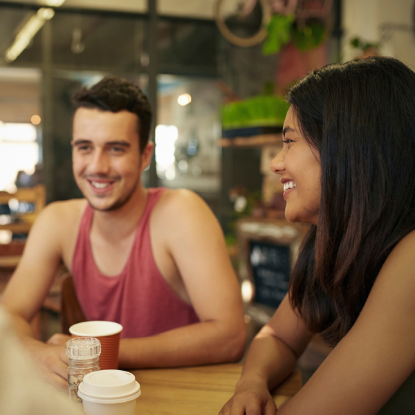 Two young adults laugh together while chatting at a cafe table, enjoying casual conversation and connection.