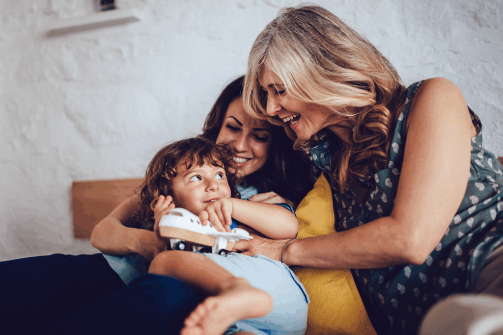 Three generations of a family share a joyful moment on a couch. A grandmother, mother, and child smiling and laughing together.