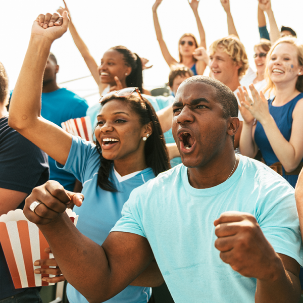 Excited sports fans cheering in the stands with popcorn and team jerseys, celebrating a thrilling play and the shared joy of live sports.
