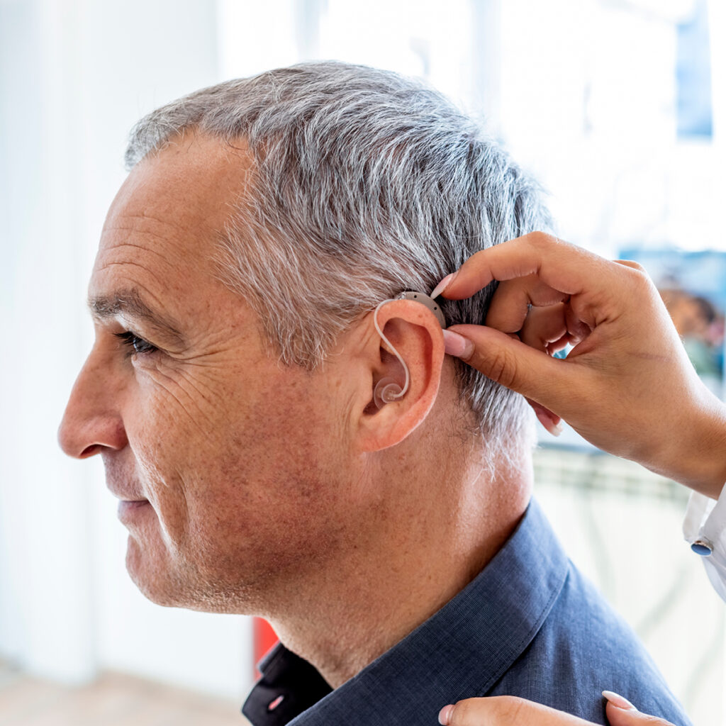 A provider places a behind-the-ear hearing aid on a man, ensuring a precise and comfortable fit.