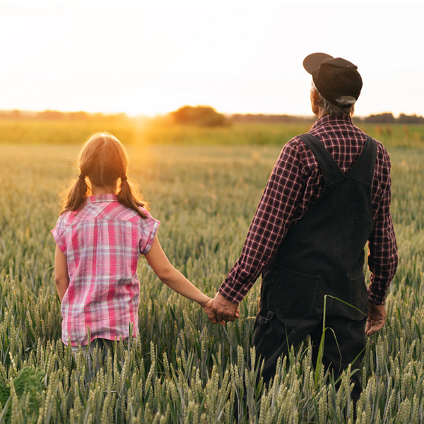 Grandfather and granddaughter holding hands in a wheat field at sunset, reflecting rural Oklahoma roots and the value of protecting hearing for life’s meaningful moments.