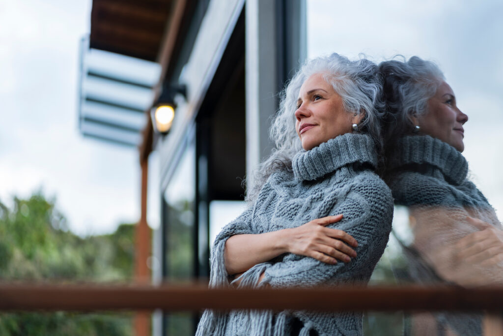 Woman in a cozy sweater standing outside and reflecting peacefully, symbolizing the connection between hearing health, brain wellness, and emotional well-being.