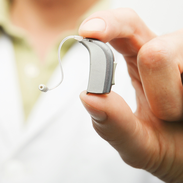 Close-up of an audiologist holding a modern behind-the-ear hearing aid, highlighting today’s advanced technology and precision fitting