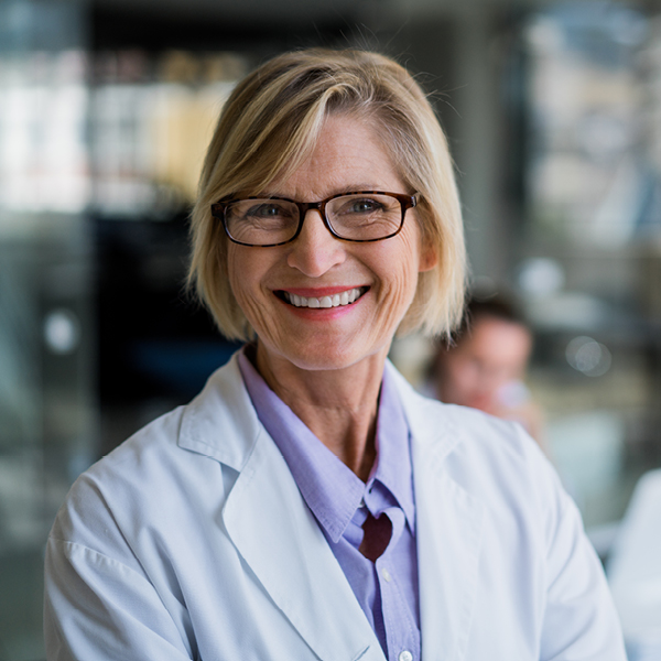 Smiling female audiologist wearing a white coat, representing professional hearing care and trusted expertise.
