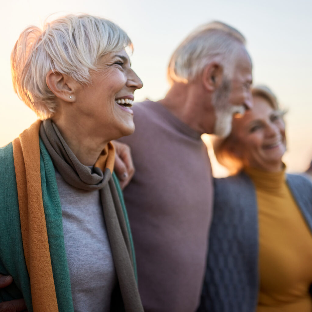 Older adults smiling together outdoors at sunset, walking arm in arm and enjoying each other’s company.