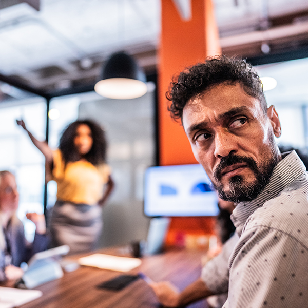 A man in a conference room turns his head to hear a colleague better during a team discussion.