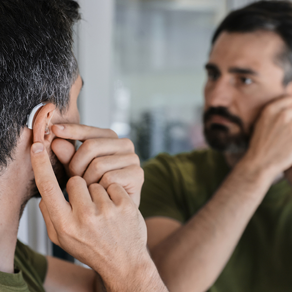 Man inserting a hearing aid at home while looking in a mirror, illustrating self-managed device use.