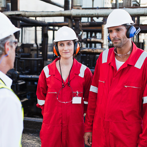 Industrial workers in protective gear wearing earmuffs while standing in a noisy work environment.
