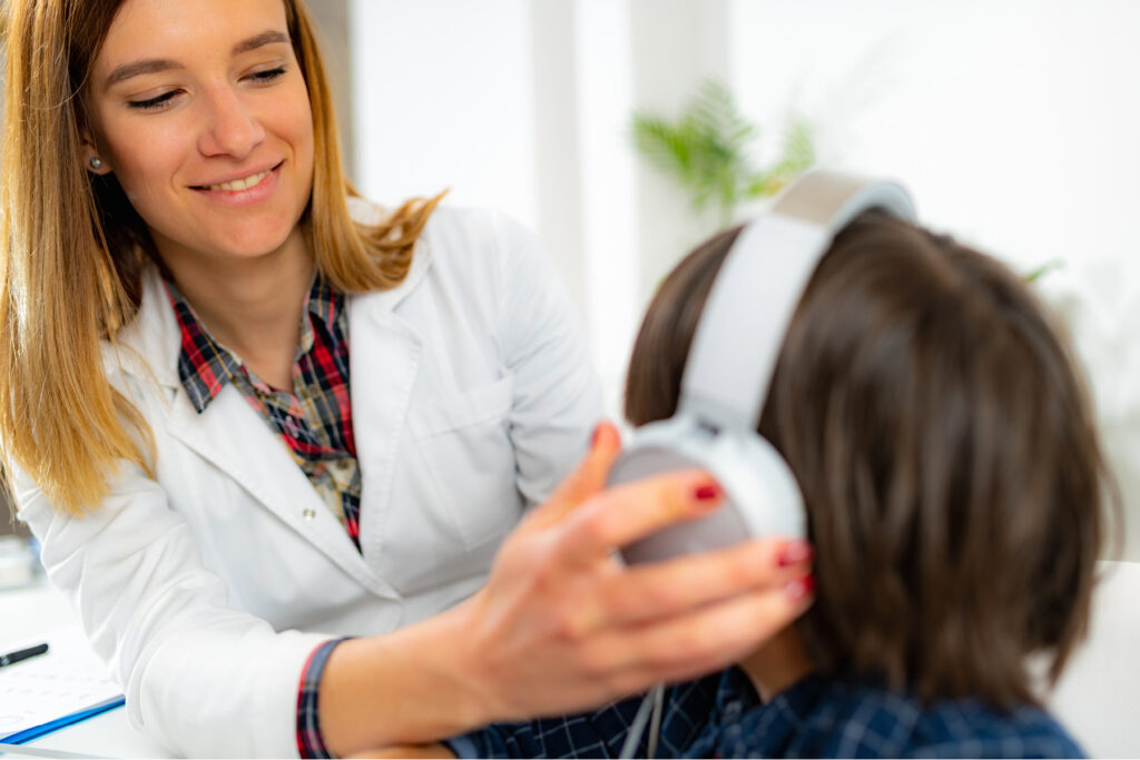 A hearing care professional gently helping a patient adjust over-ear headphones during a hearing evaluation.