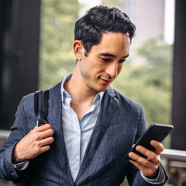 An adult wearing a discreet hearing device while looking at a smartphone during daily life.