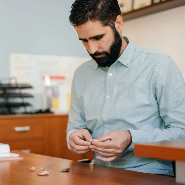 Hearing care professional examining and adjusting a hearing aid at a clinic desk.