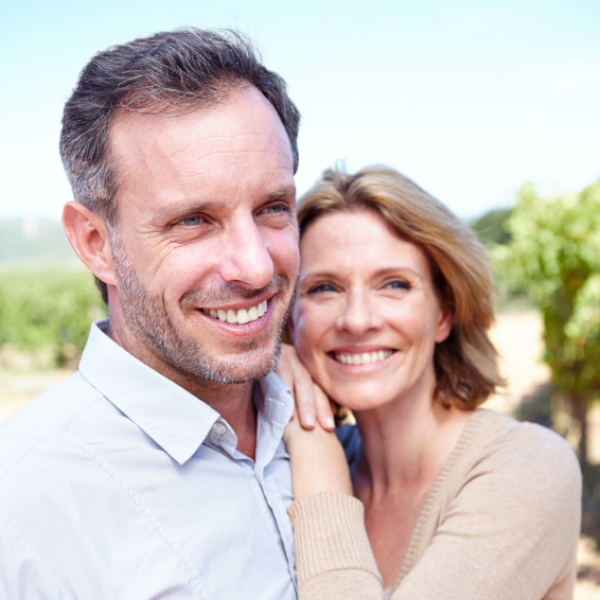 Middle-aged couple smiling outdoors, representing healthy aging and staying connected through clear communication.