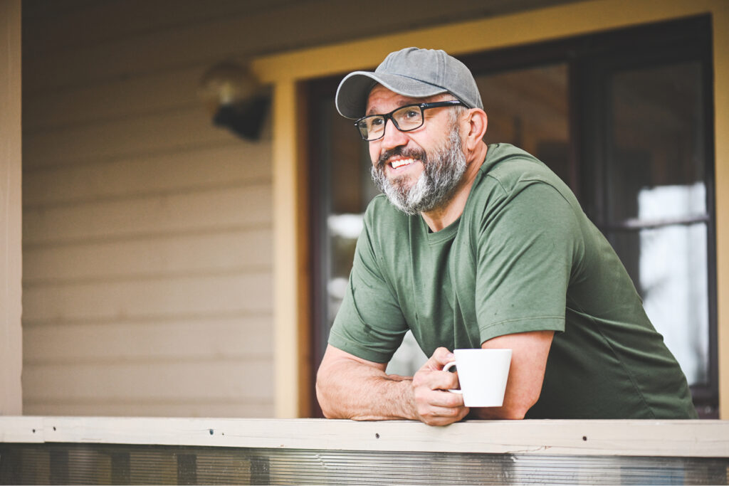 Man in his 50s relaxing on a porch with a coffee, illustrating confidence, comfort, and everyday well-being.