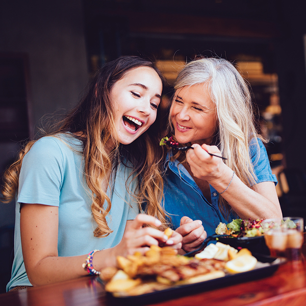 Older adult and younger family member enjoying a meal together and laughing during conversation in a restaurant setting.