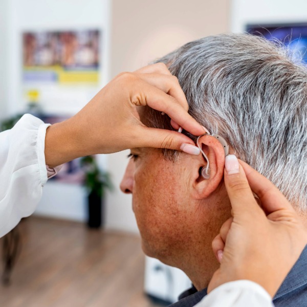 Hearing care professional adjusting a behind-the-ear hearing aid on an older adult during a routine follow-up appointment.