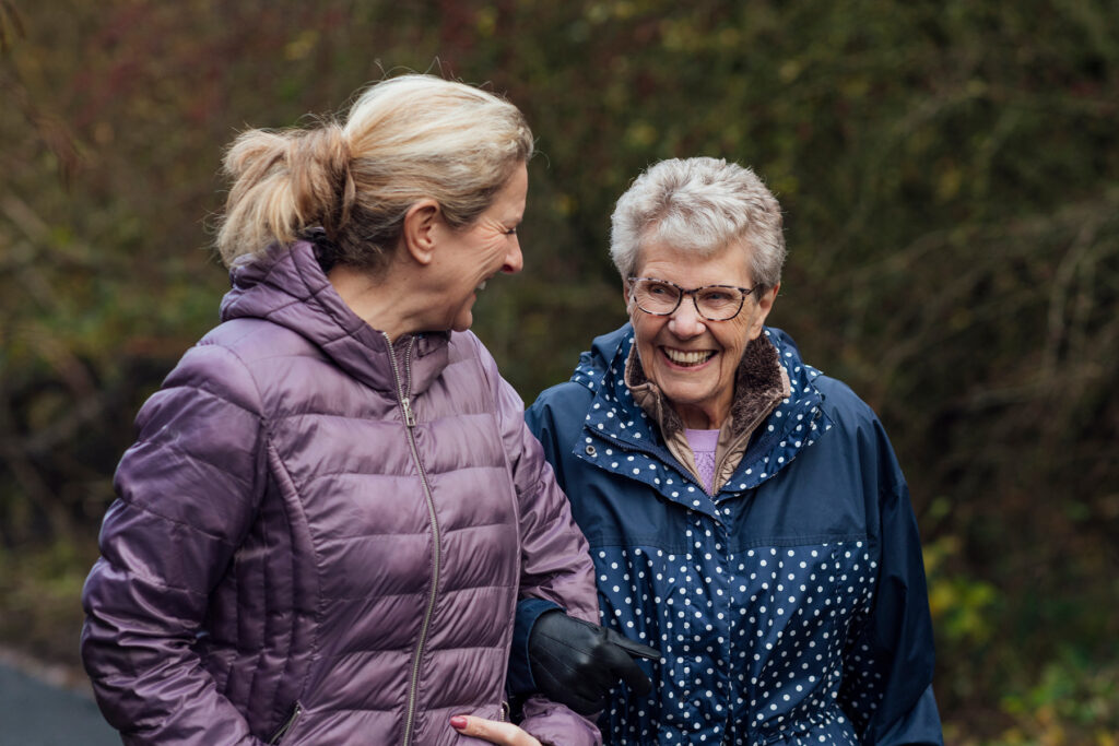 Older woman walking outdoors with a companion, smiling and engaged, representing healthy aging and the connection between hearing and brain health.