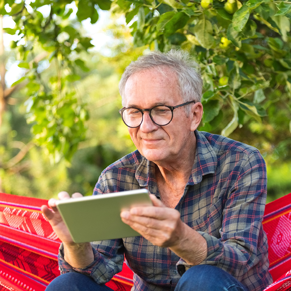 Older adult man wearing glasses using a tablet outdoors, illustrating aging, vision changes, and hearing health considerations.