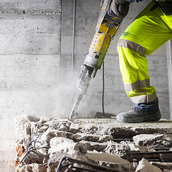 Worker using a jackhammer on concrete shows high noise exposure on construction sites and the importance of proper hearing protection.