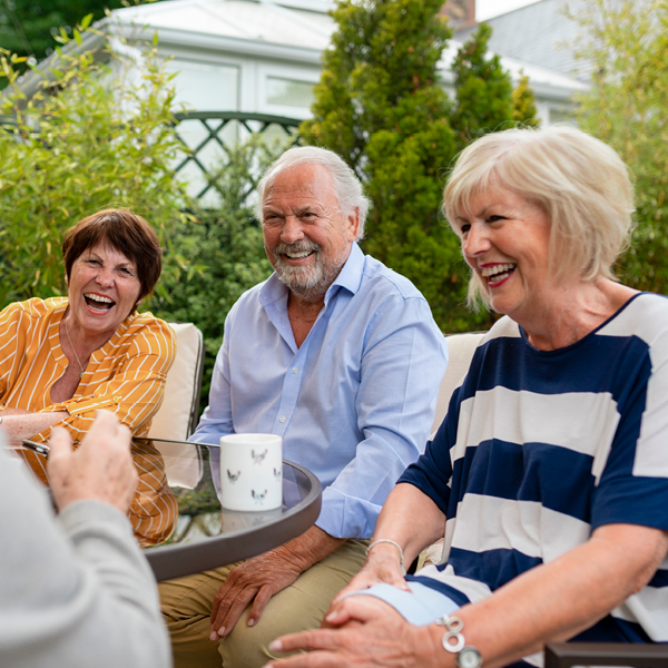Three adults laughing together at an outdoor table, illustrating how clear hearing helps maintain social engagement and confidence in group settings.