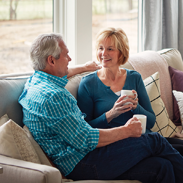 A couple sitting together on a couch at home, enjoying conversation and connection, representing how healthy hearing supports daily independence.