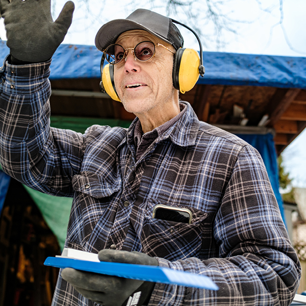 Farmer wearing yellow earmuffs and protective gloves while working outdoors with equipment, demonstrating proper hearing protection to prevent farm noise hearing loss.