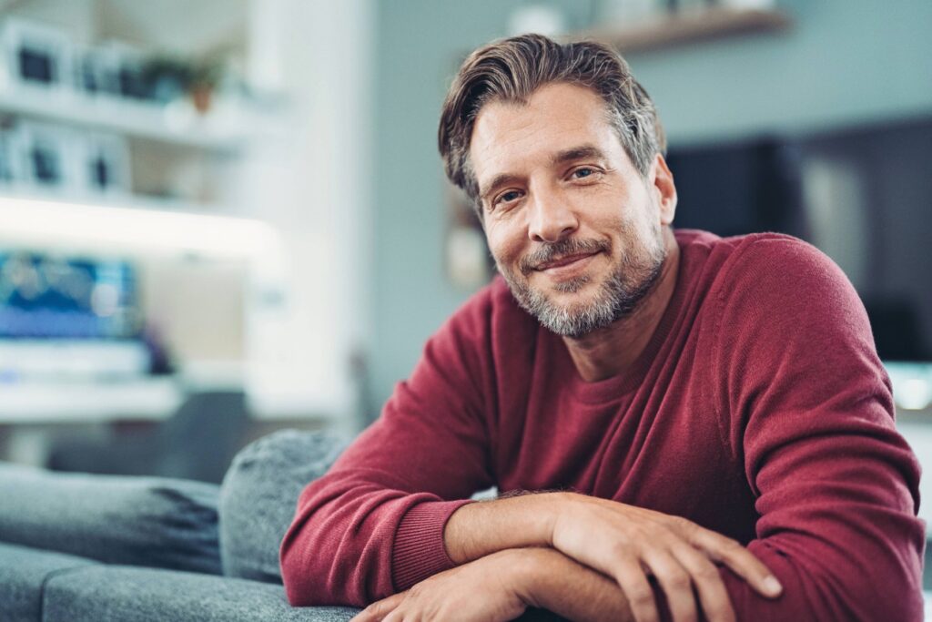Middle-aged man sitting comfortably at home and smiling, representing relief from tinnitus and improved quality of life through tinnitus habituation and professional hearing care.