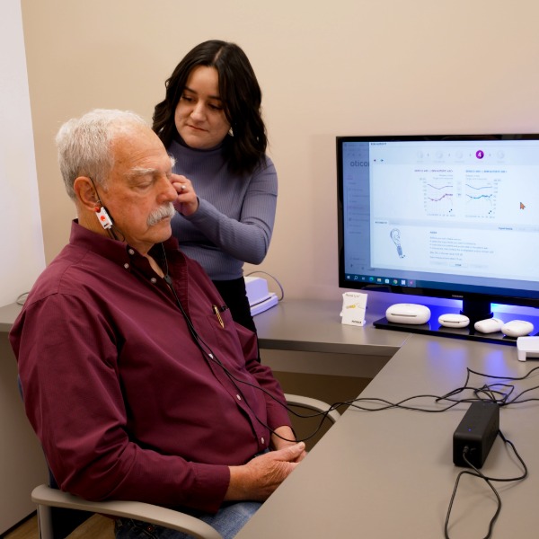 Hearing care professional performing real-ear measurement to verify hearing aid settings during a certified hearing care appointment in a clinical testing room.