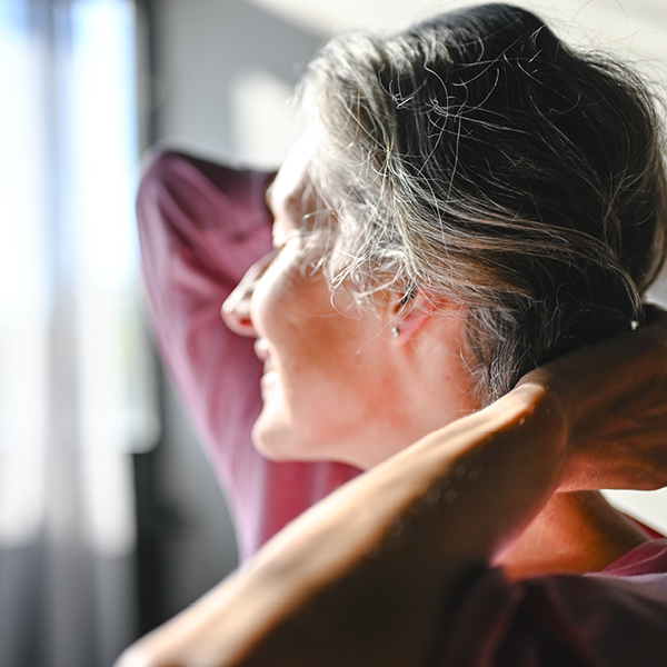 Woman adjusting a custom behind-the-ear hearing aid showing comfortable personalized hearing support.