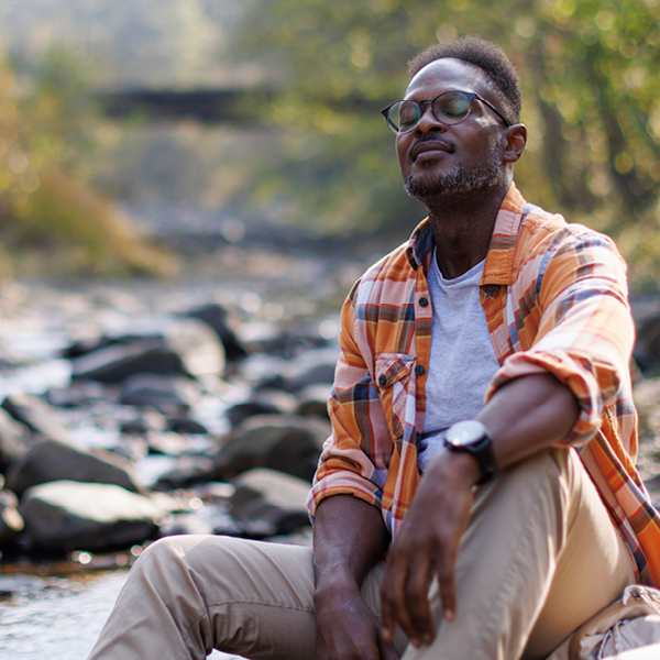 Man relaxing by a river enjoying quiet moments and natural sound clarity with improved hearing.
