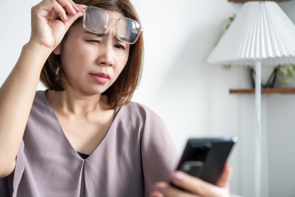 Woman squinting at her phone and adjusting glasses, illustrating vision decline and its impact on daily tasks and cognitive effort