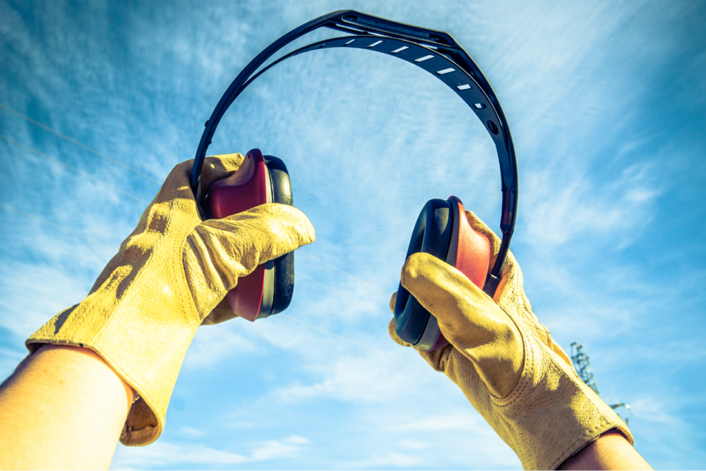 Industrial noise-reduction earmuffs held up against the sky, representing hearing protection for railroad and train workers.