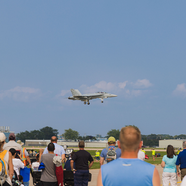 Crowd watching a jet aircraft landing at an air show without visible hearing protection