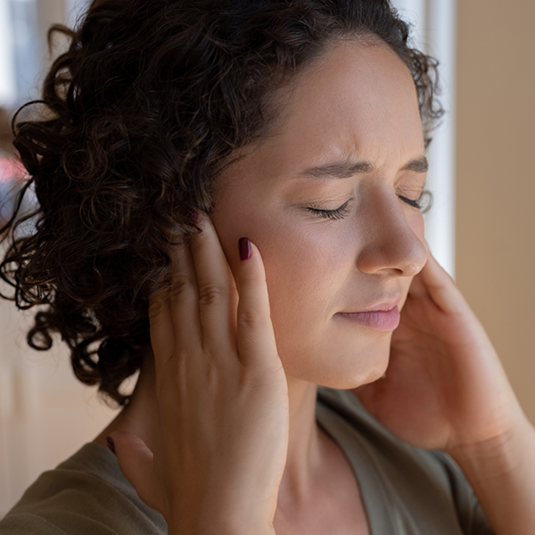 Woman pressing her ears with eyes closed, representing ringing in the ears and tinnitus symptoms.