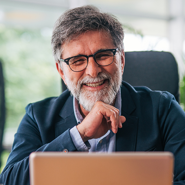 Older man smiling while using a laptop at home, researching tinnitus relief technology and sound therapy options.