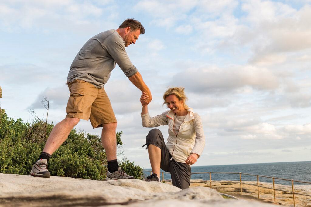 Active couple hiking outdoors and helping each other, symbolizing improved connection and energy after addressing hearing loss and listening fatigue