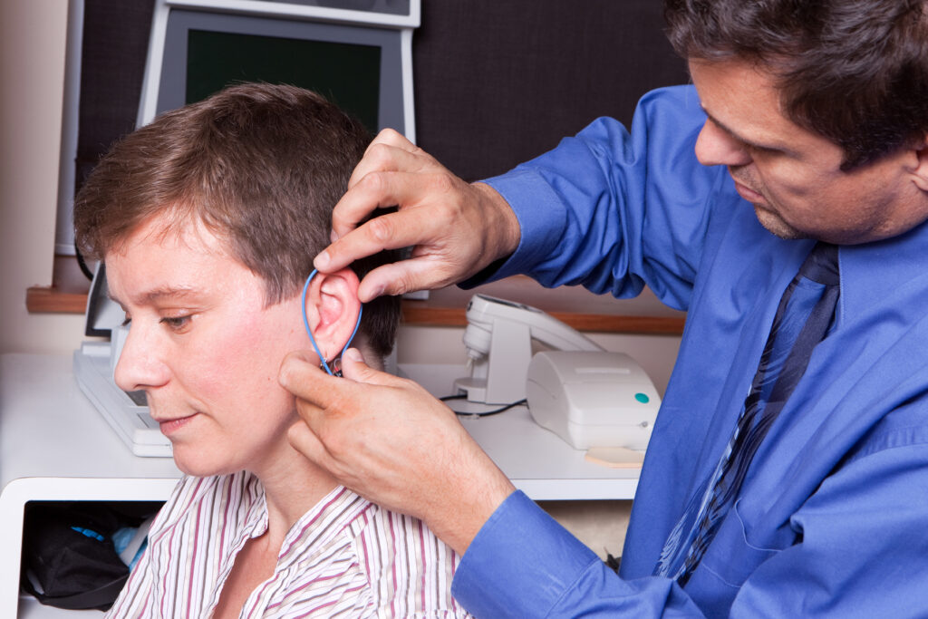 An audiologist inserting a probe tube into a patient's ear canal to perform real-ear measurement and verify hearing aid amplification accuracy