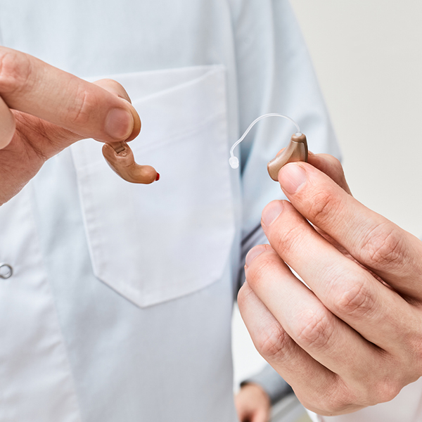 Hearing care professional holding two styles of hearing aids, showing the difference between an in-the-ear and receiver-in-canal device