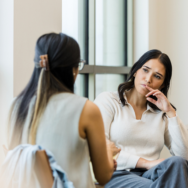 An adult woman listens with concern as another woman speaks during a serious one-on-one conversation indoors